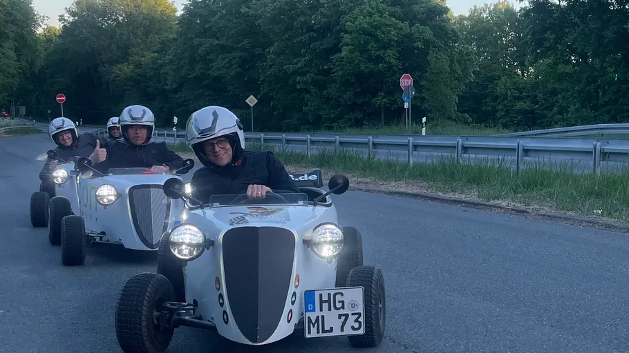 Drei Personen fahren Mini-Autos auf Straße.