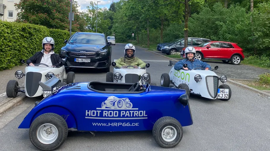 Three people driving mini hot rods on street.