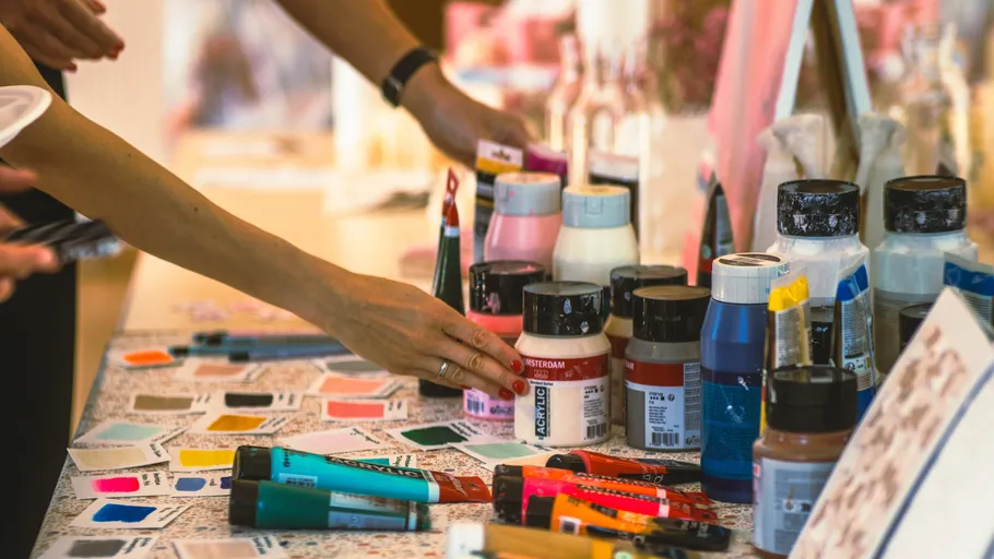 Hands reaching for paint bottles on table.