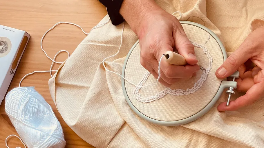 Person sticht Nadel in Stickrahmen.