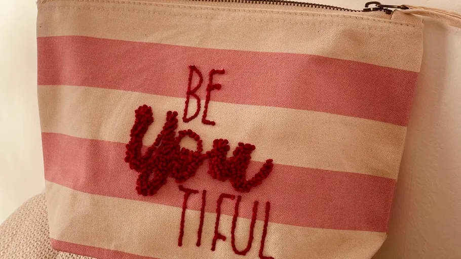 Canvas-Tasche mit gesticktem Text und Streifen.
