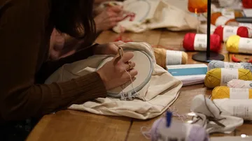 Person embroidering with yarn on a wooden table.
