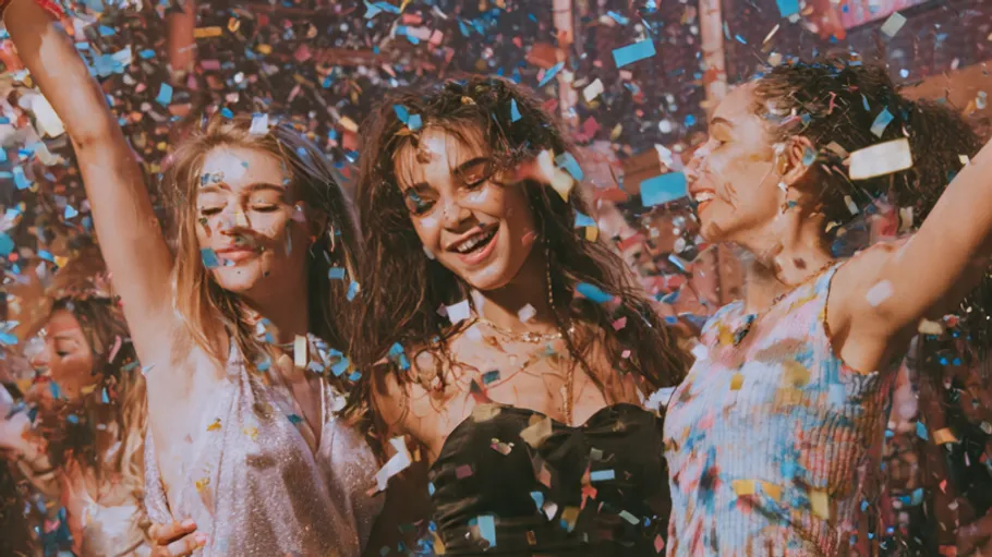 Three women dancing amid falling confetti.