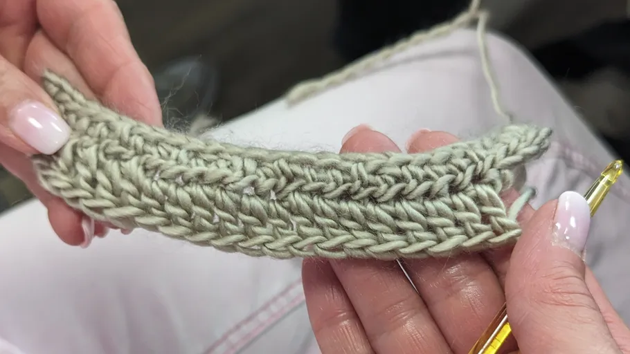 Hände halten teilweise gestricktes Garnstück.