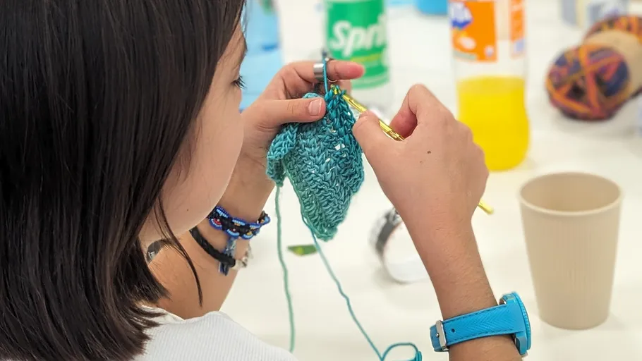 Person strickt mit blauem Garn am Tisch.