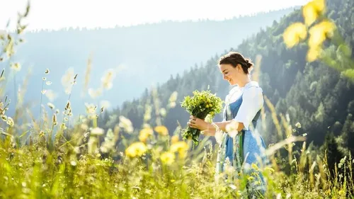 Frau hält Kräuter auf sonniger Wiese.