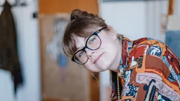 Person mit Brille lächelt drinnen.