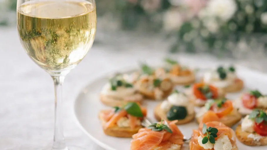 Glass of white wine with appetizers on plate.