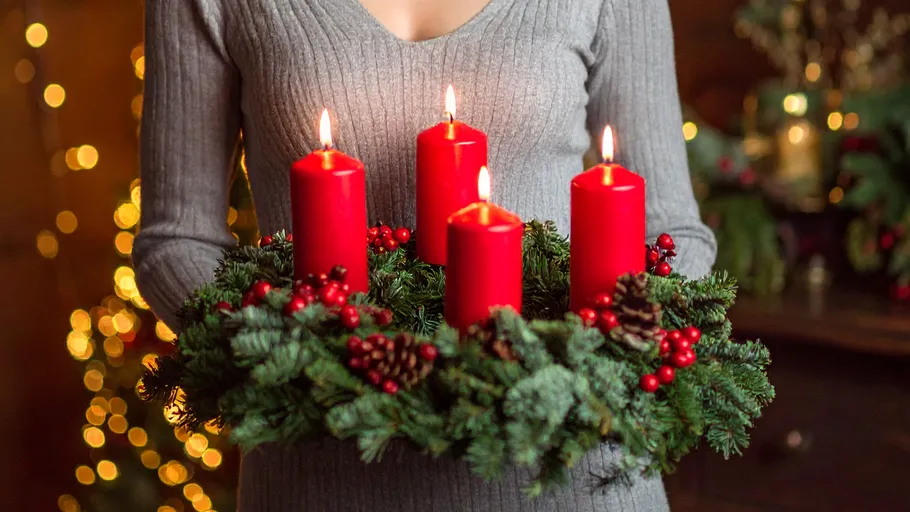 Person holding wreath with four red candles.