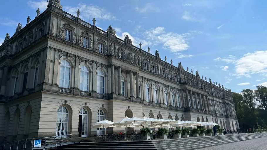 Großes historisches Gebäude mit Außenbestuhlung, sonniger Tag.