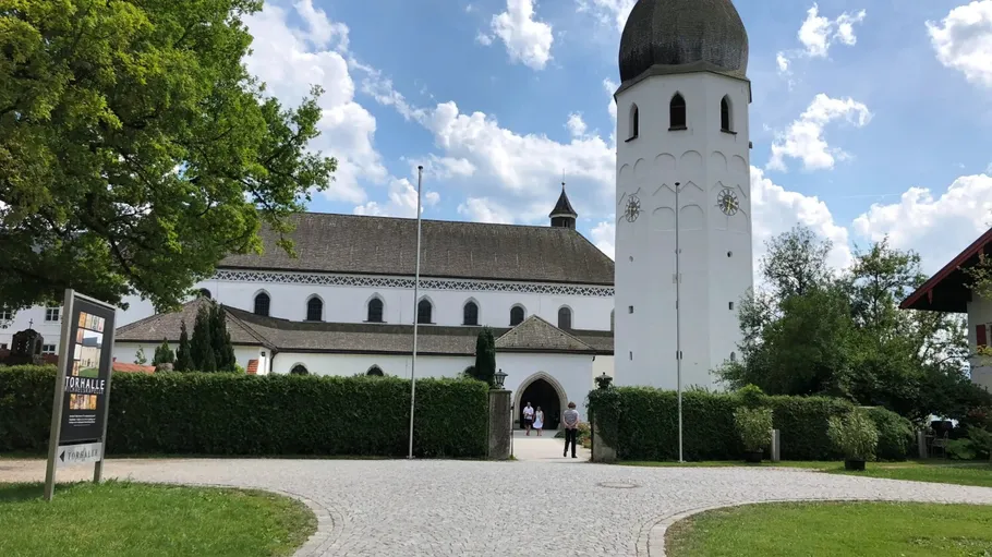 Weiße Kirche mit hohem Turm, umgeben von Grün.