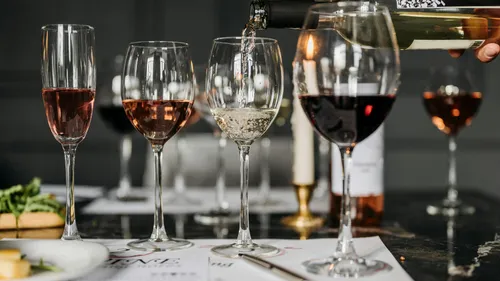 Wine glasses filled, bottle pouring, dim setting.