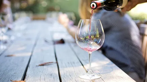 Wein wird in Glas auf Gartentisch eingeschenkt.