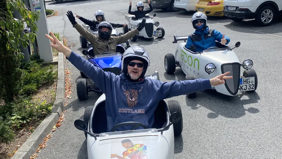 People driving small cars in a parking lot.