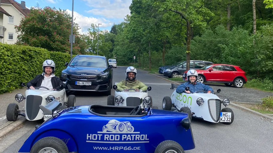 Three people driving small cars on a street.