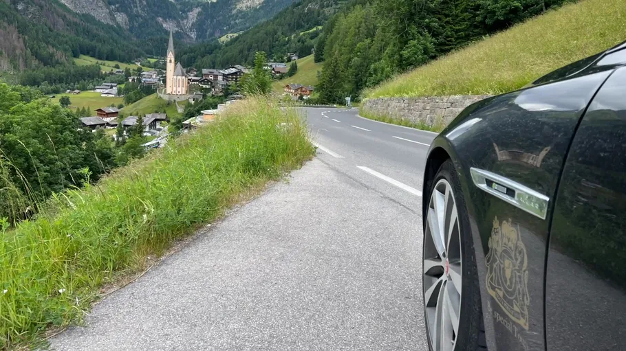 Car parked on mountain road, church in distance.