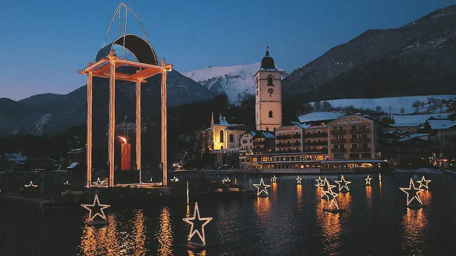 Christmas lights float on water with mountain backdrop.