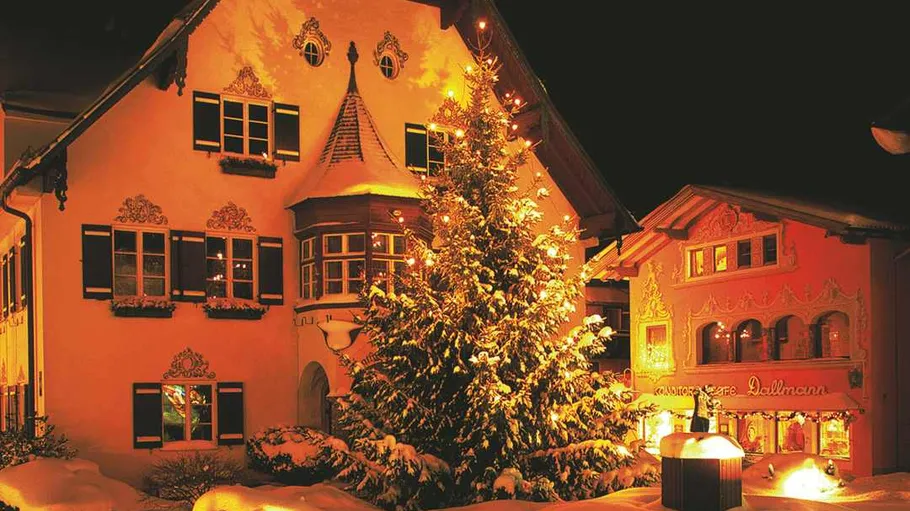 Illuminated Christmas tree beside festively decorated houses.