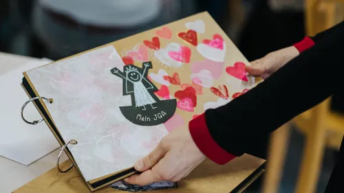 Person holding scrapbook with hearts and drawing.
