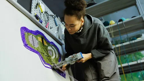 Person using tufting gun on canvas, colorful design.