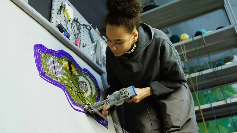 Person using tufting gun on canvas, colorful design.