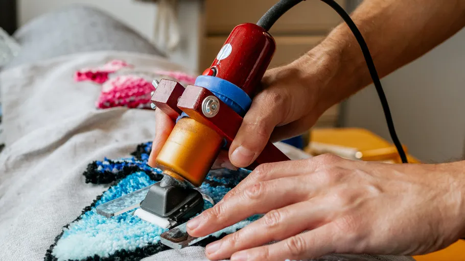 Person using tufting gun on fabric design.