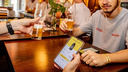 Menschen stoßen mit Bier an, prüfen Smartphone-App.