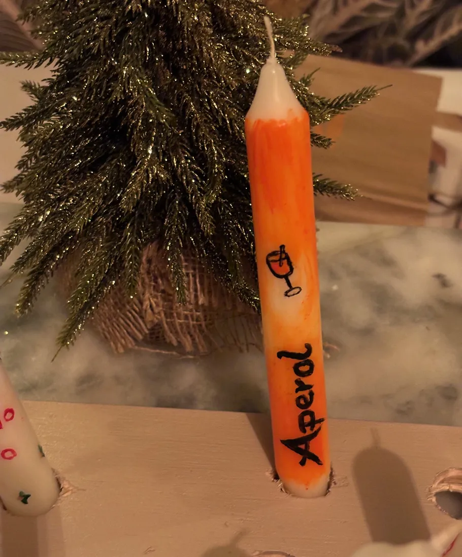 Orange candle labeled Aperol beside small tree.