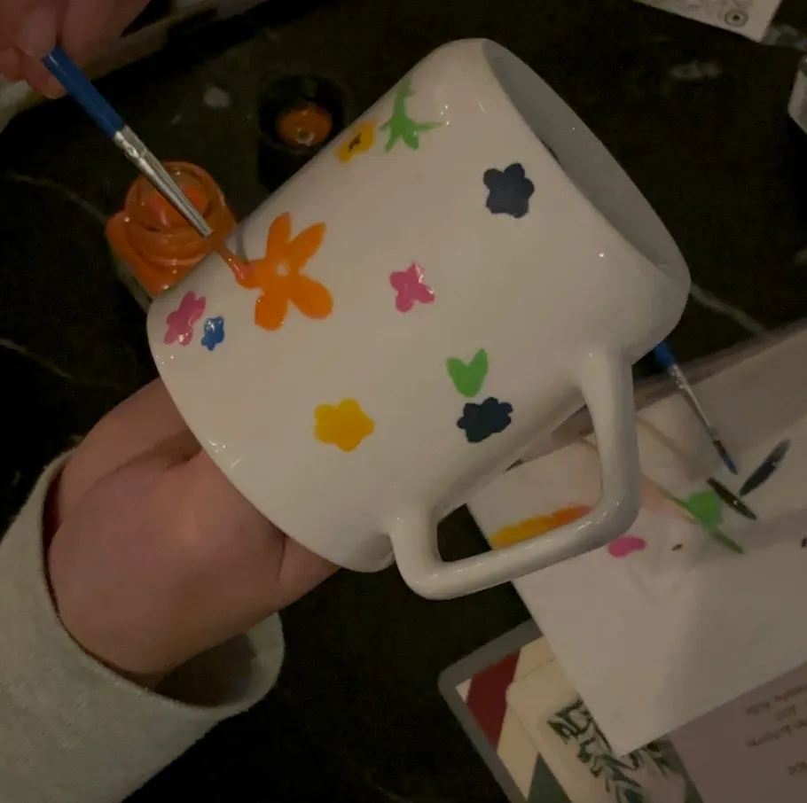 Person painting colorful flowers on white mug.