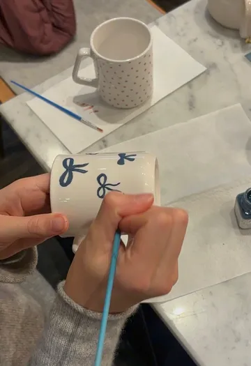 Person malt blaue Schleifen auf eine Tasse.