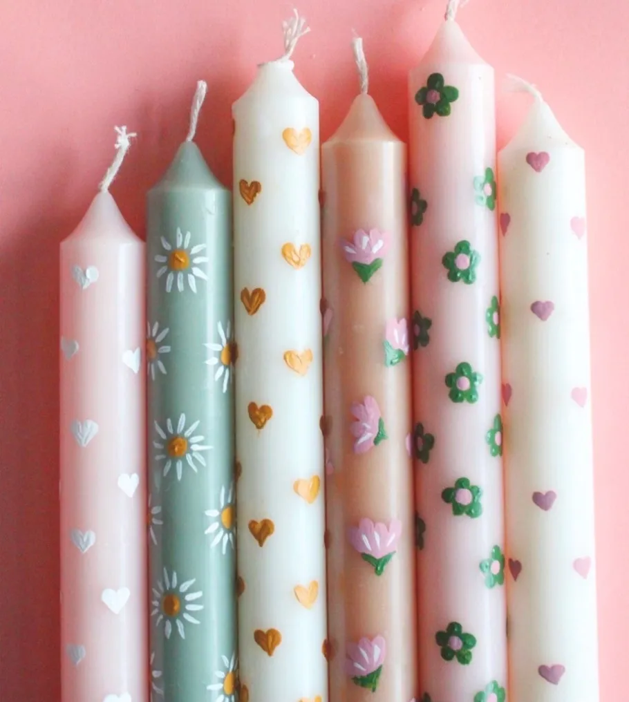 Decorative candles with floral designs on pink surface.