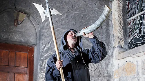 Man blowing horn, holding axe, stone building.