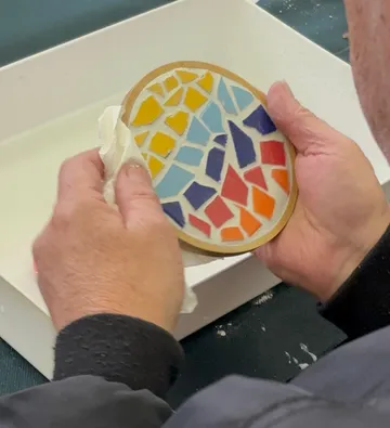 Hände reinigen buntes Mosaik auf rundem Brett.