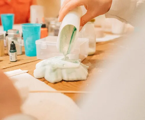 Hand pouring green liquid into mold, crafting table.