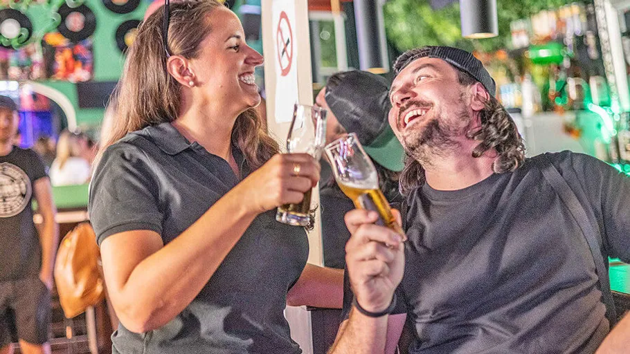 Zwei Menschen lachen und halten Getränke in einer Bar.