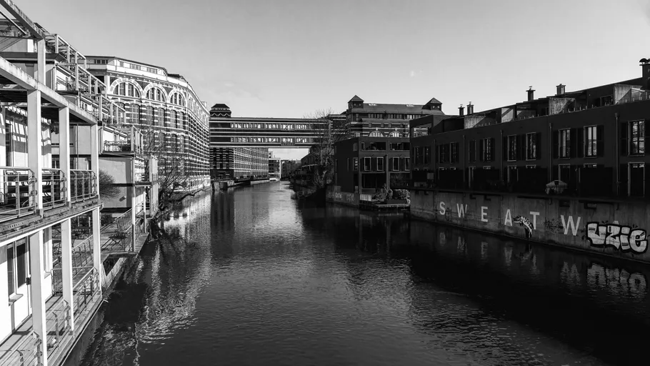 Kanal flankiert von Industriebauten, Graffiti sichtbar.