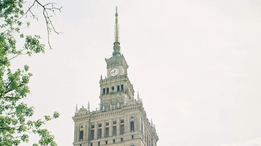 Tall building with clock, tree branches foreground.