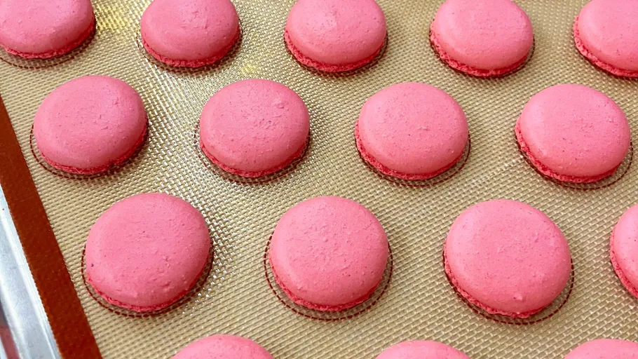 Pink macarons resting on a baking sheet.