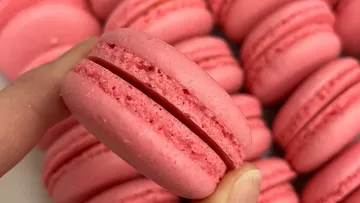 Pink macarons held by fingers among others.
