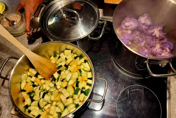 Kochen von lila Blumenkohl und Kürbis auf Herd.