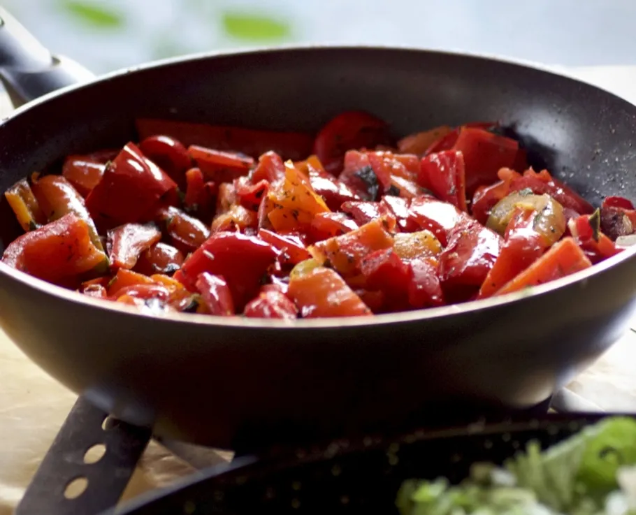 Chopped red peppers cooking in a frying pan.