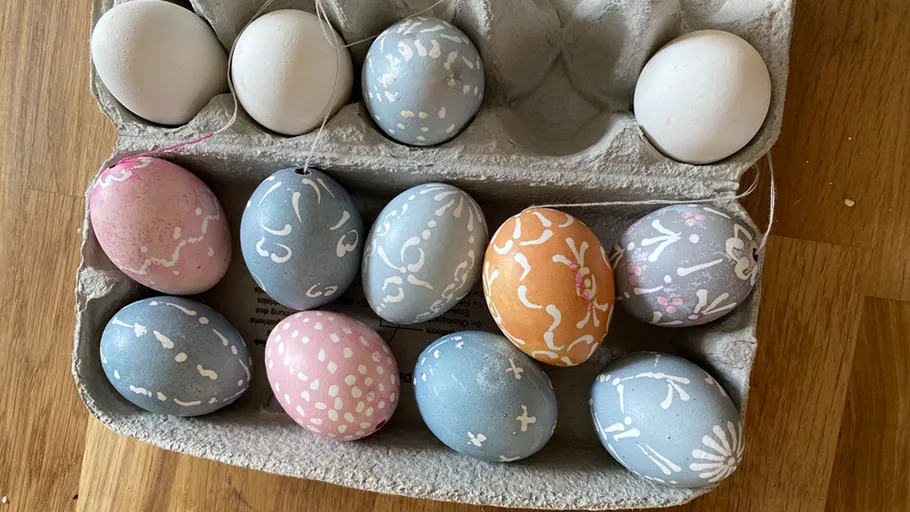 Decorated eggs in a carton on wood floor.