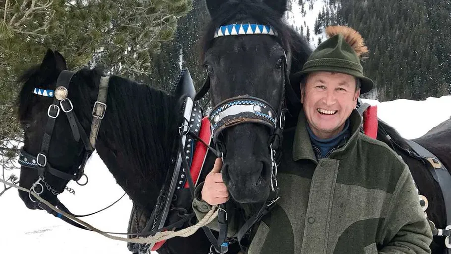 Smiling man with two harnessed horses in snow.