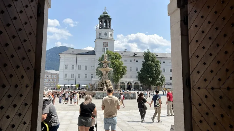 Menschen gehen im Salzburger Hof, Uhrturm sichtbar.