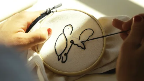 Hands embroidering bird outline on fabric.