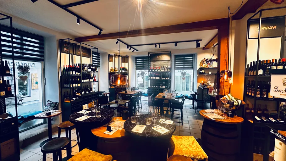 Cozy wine bar with tables and shelves of bottles.