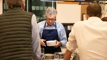 Mann mit Schürze hält Schüssel in Küche.