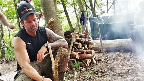 Mann schnitzt Holz auf einem Waldcampingplatz.