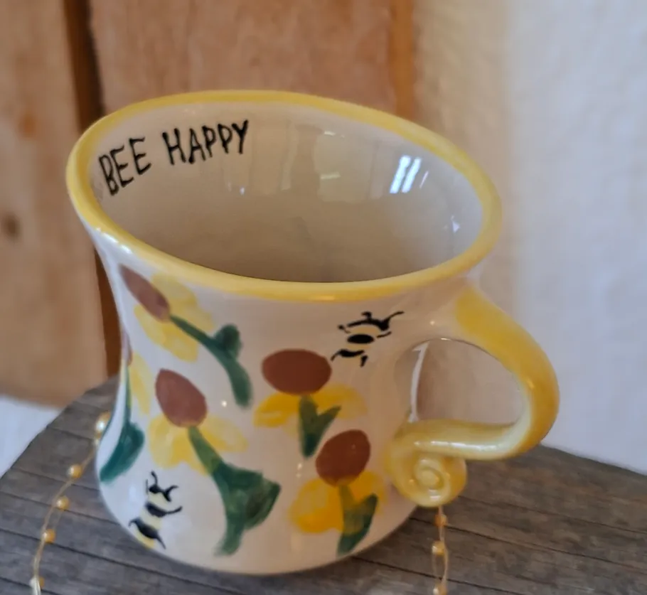Ceramic mug with flowers and bees, on table.