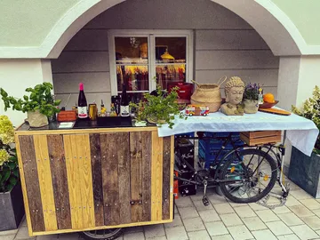 Holzbar auf Fahrrad mit Pflanzen und Getränken, draußen.
